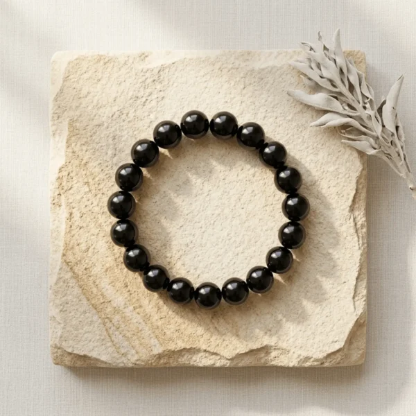 Black obsidian 10mm crystal bracelet with round glossy black beads on neutral stone background