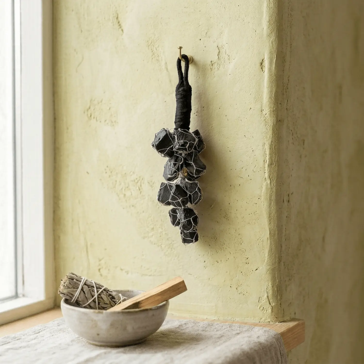 Black Tourmaline crystal hanger displayed near a window with cleansing accessories