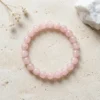 Rose Quartz crystal bracelet with polished 8mm pink gemstone beads displayed flat on textured beige stone surface