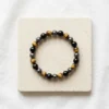 Triple Protection Combination bracelet with polished Tiger Eye, Hematite and Black Obsidian beads displayed on stone background