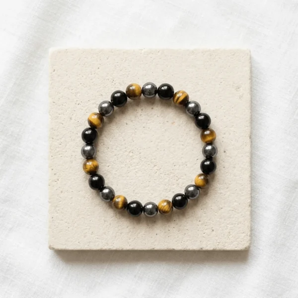 Triple Protection Combination bracelet with polished Tiger Eye, Hematite and Black Obsidian beads displayed on stone background