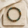 Wealth Combination crystal bracelet with polished Green Aventurine Tiger Eye and Pyrite gemstone beads displayed on textured stone surface