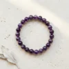 Amethyst 8mm crystal bracelet with round purple beads on neutral stone background