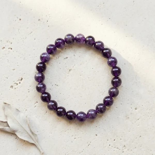 Amethyst 8mm crystal bracelet with round purple beads on neutral stone background