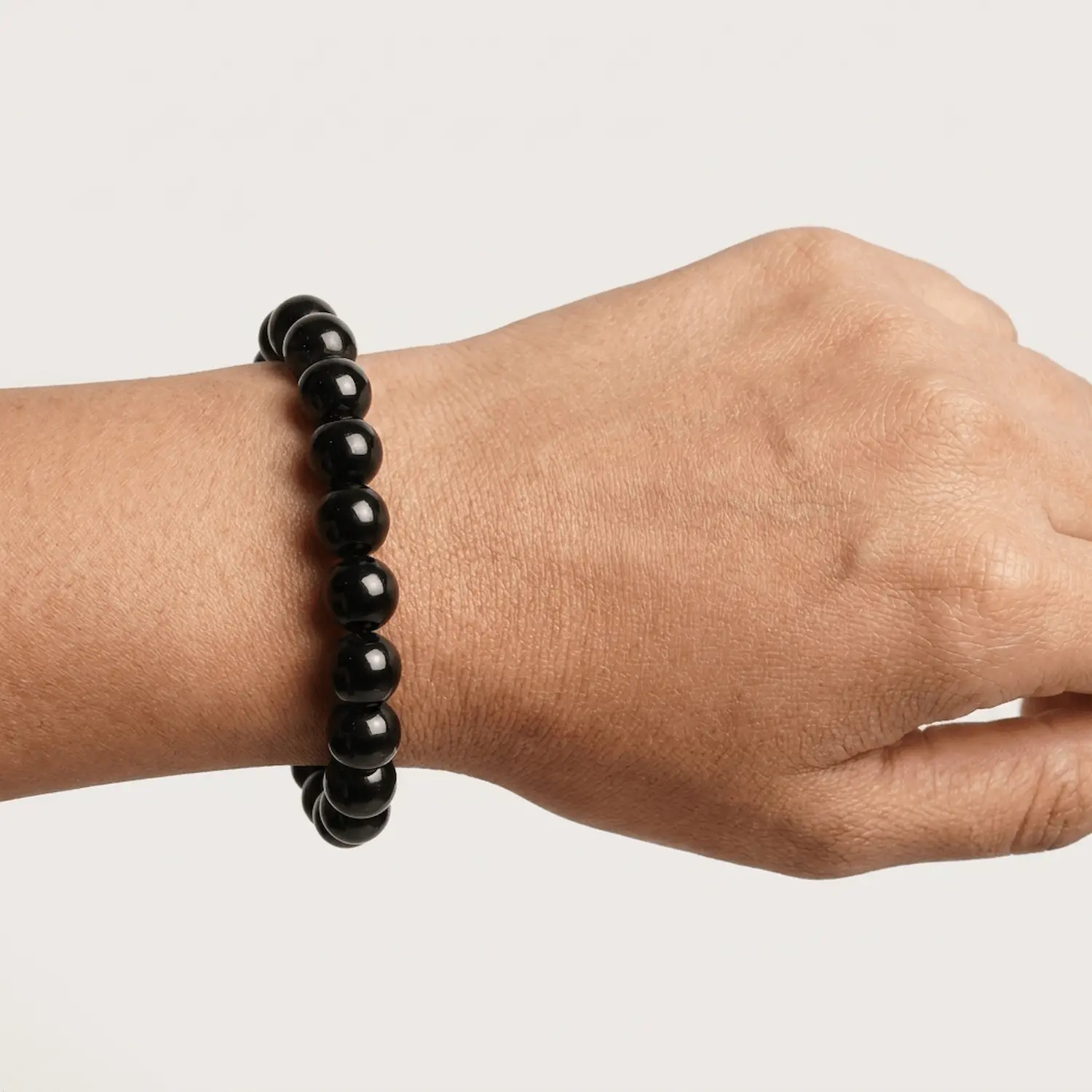 Close-up of 10mm black obsidian crystal bracelet on wrist showing bead shine and size