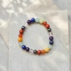 Seven chakra crystal bracelet with multicoloured natural stone beads on neutral stone background