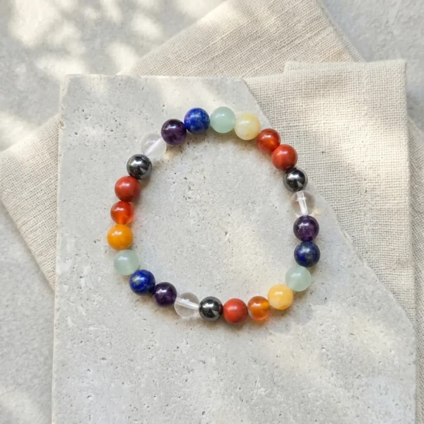 Seven chakra crystal bracelet with multicoloured natural stone beads on neutral stone background