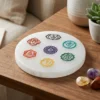 Round selenite plate with seven coloured chakra symbols on a wooden surface